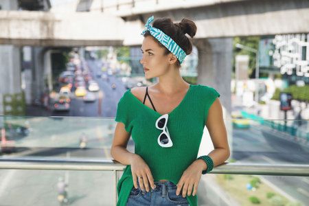 Stylish model wearing green shirt and bandana is posing on the bridge beside highway
