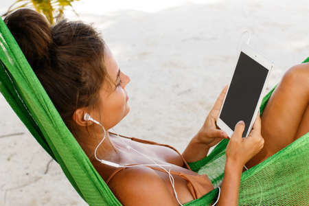Woman in hammock on the beach and using tablet PCの写真素材