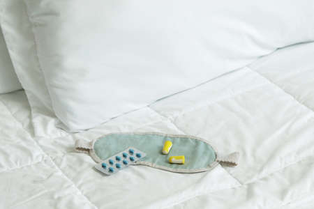 Earplugs, blindfold and sleeping pills on bedの写真素材