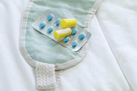 Earplugs, blindfold and sleeping pills on bedの写真素材