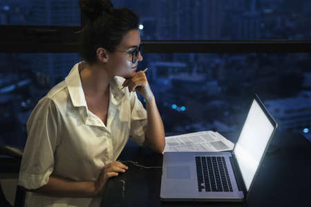 Woman is working with laptop at home during night.の写真素材