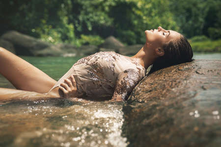 Sexy woman wearing shiny swimsuit is relaxing on the rocky beachの写真素材