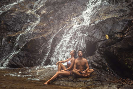 Couple is sitting under the cold waterfall during hot dayの写真素材