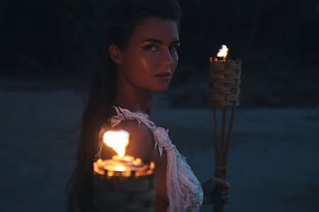 Bride in beautiful wedding dress is holding torchlight on the beachの写真素材