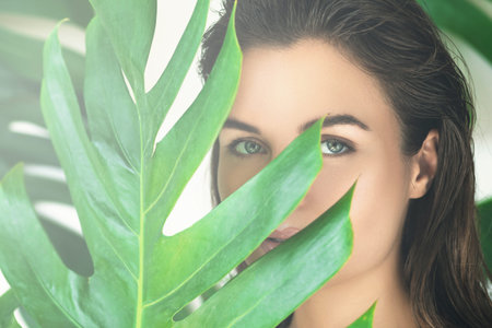 Portrait of young and beautiful woman with perfect smooth skin in tropical leaves.