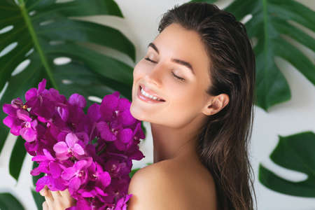 Young and beautiful woman with perfect smooth skin is holding orchid flowersの写真素材