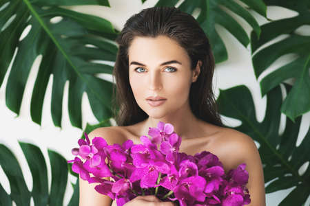 Young and beautiful woman with perfect smooth skin is holding orchid flowersの写真素材