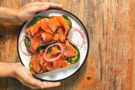 Female hands and delicious toasts with a smoked salmon, avocado and basil leavesの写真素材