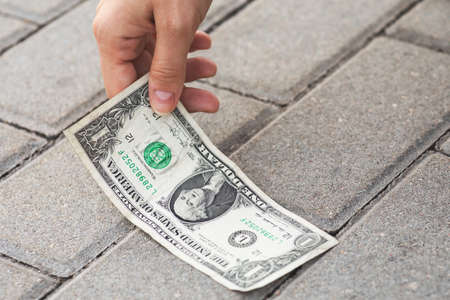 Woman is picking one dollar banknote from the ground.の写真素材
