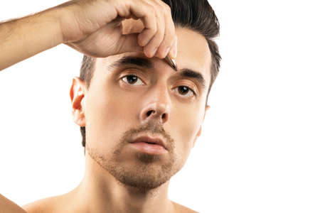 Young guy holding tweezers near his eyebrow for thats shape correctionの写真素材