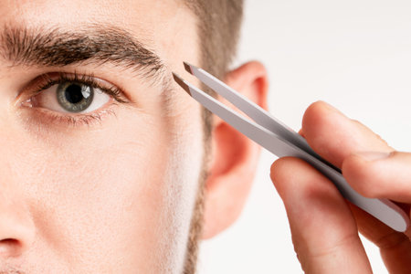 Male eye and tweezers for eyebrow grooming and shape correction