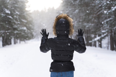 Woman wearing down jacket with a hood walking in park during cold winter dayの写真素材