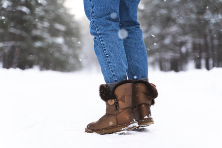 Woman wearing sheepskin boots walking by snowy roadの写真素材
