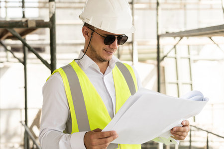 Man architect wearing safety vest with a blueprints on a construction site