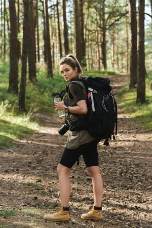 Female hiker with big backpack and reusable bottle for water in green forest