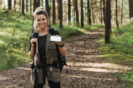 Female hiker showing smartphone with blank display in green forestの写真素材