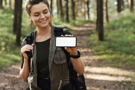 Female hiker showing smartphone with blank display in green forestの写真素材