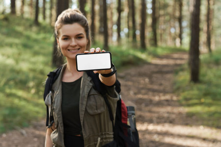 Female hiker showing smartphone with blank display in green forest