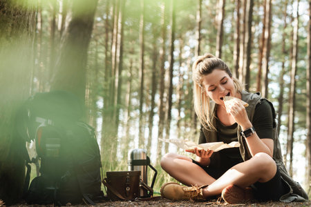 Female hiker during small halt eating sandwich in green forestの写真素材