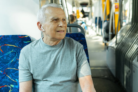Elderly man is using wireless earbuds during ride in public transportの写真素材