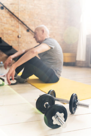 Dumbbells and elderly man relaxing after his fitness workout at homeの写真素材