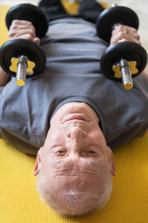 Elderly man exercising with a dumbbells during his workout in home gymの写真素材