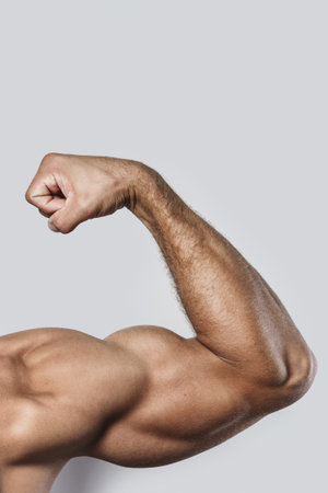 Muscular arm of young bodybuilder on gray backgroundの写真素材