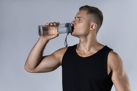 Athletic man drinking water against gray backgroundの写真素材