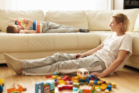 Boy lying on the sofa and his mother sitting on the floor after game with a construct toyの写真素材