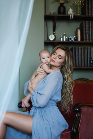 Young beautiful mother wearing luxury grey dress holding her baby on hands
