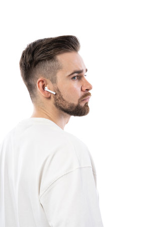 Handsome bearded man in white clothes using wireless earbuds on white backgroundの写真素材