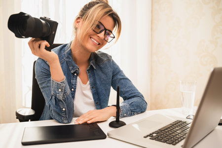 Happy woman photographer with a mirrorless camera at the workplaceの写真素材