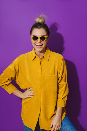 Young cheerful girl wearing yellow shirt and sunglasses against purple backgroundの写真素材