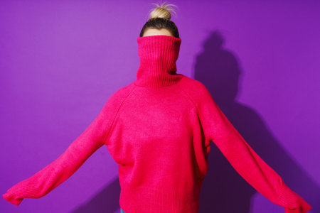 Funny woman hiding her face inside a warm and cozy polo neck sweater against purple backgroundの写真素材