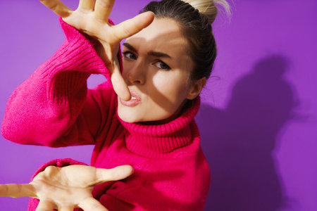 Young woman in wearid pose wearing warm polo neck sweater against purple backgroundの写真素材