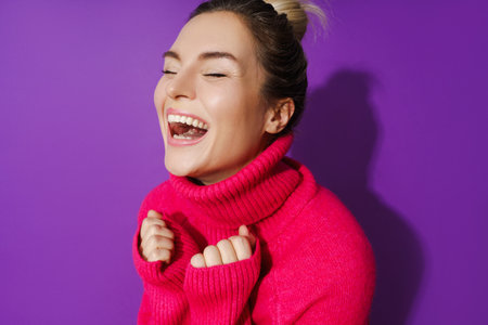 Wide-angle portrait of cheerful woman wearing warm polo neck sweater against purple backgroundの写真素材