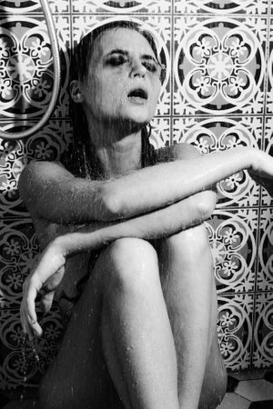 Portrait of sad and wet woman with smudged makeup on her face under the showerの写真素材