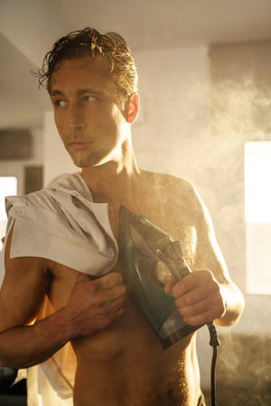 Handsome young man ironing his chest with clothes ironの写真素材