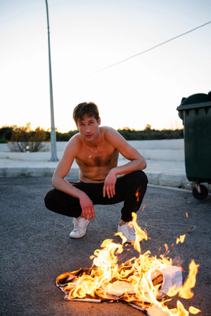 Adult man pyromaniac burning his shirt on the street