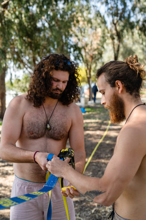 Two men setting up slacklining equipment in city park during summer day