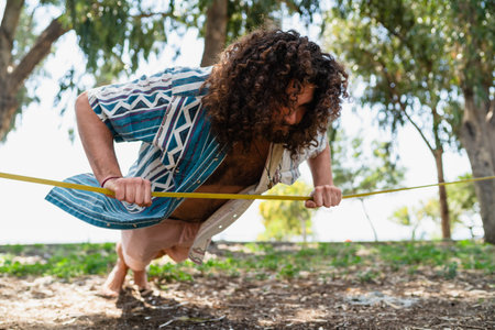 Confident young man doing pushups and balancing on the slackline in city park
