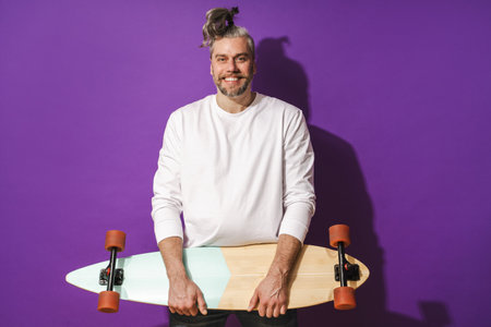 Cheerful middle aged man with longboard wearing white sweatshirt against purple backgroundの写真素材