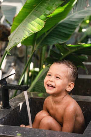Adorable toddler boy playing and bathing in stone sink outdoors