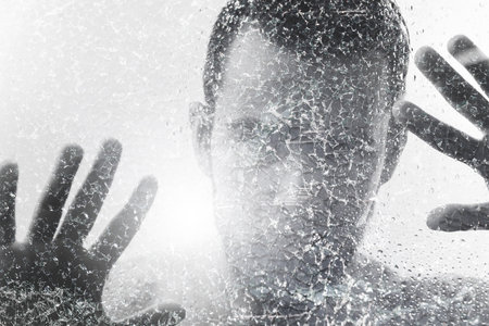 Man behind wet and cracked glass. Concepts of mental disorder or other social issues affecting human personalityの写真素材