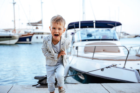 Excited stylish boy running near yacht in marinaの写真素材