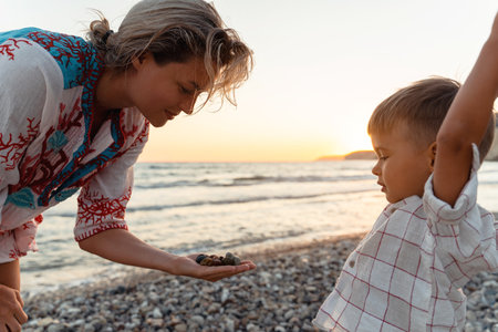 Mother and her cute little son collecting pebbles on shingle beachの写真素材