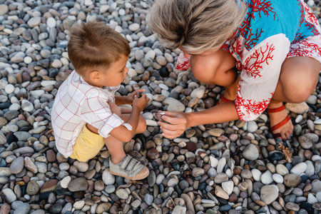 Mother and her cute little son collecting pebbles on shingle beachの写真素材