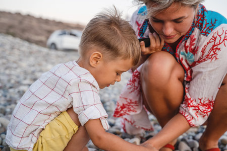 Mother and her cute little son collecting pebbles on shingle beachの写真素材