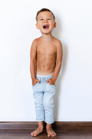 Happy cheerful little boy wearing jeans posing against white wallの写真素材