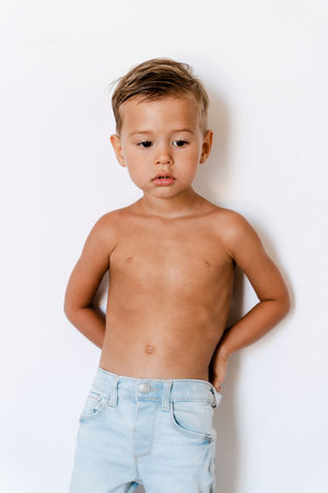 Cute little boy wearing blue jeans posing against white background like fashion modelの写真素材